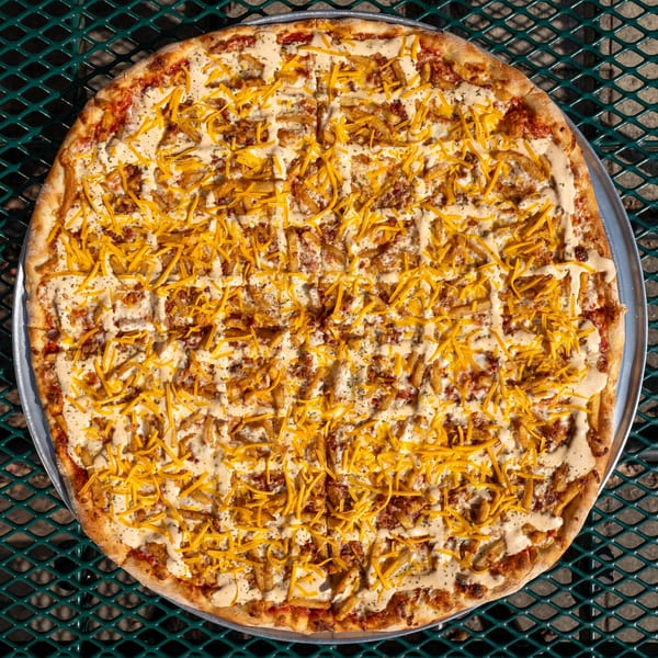 Tommyboy's Pizza with fries, shredded cheese, and a creamy sauce on a metal table.
