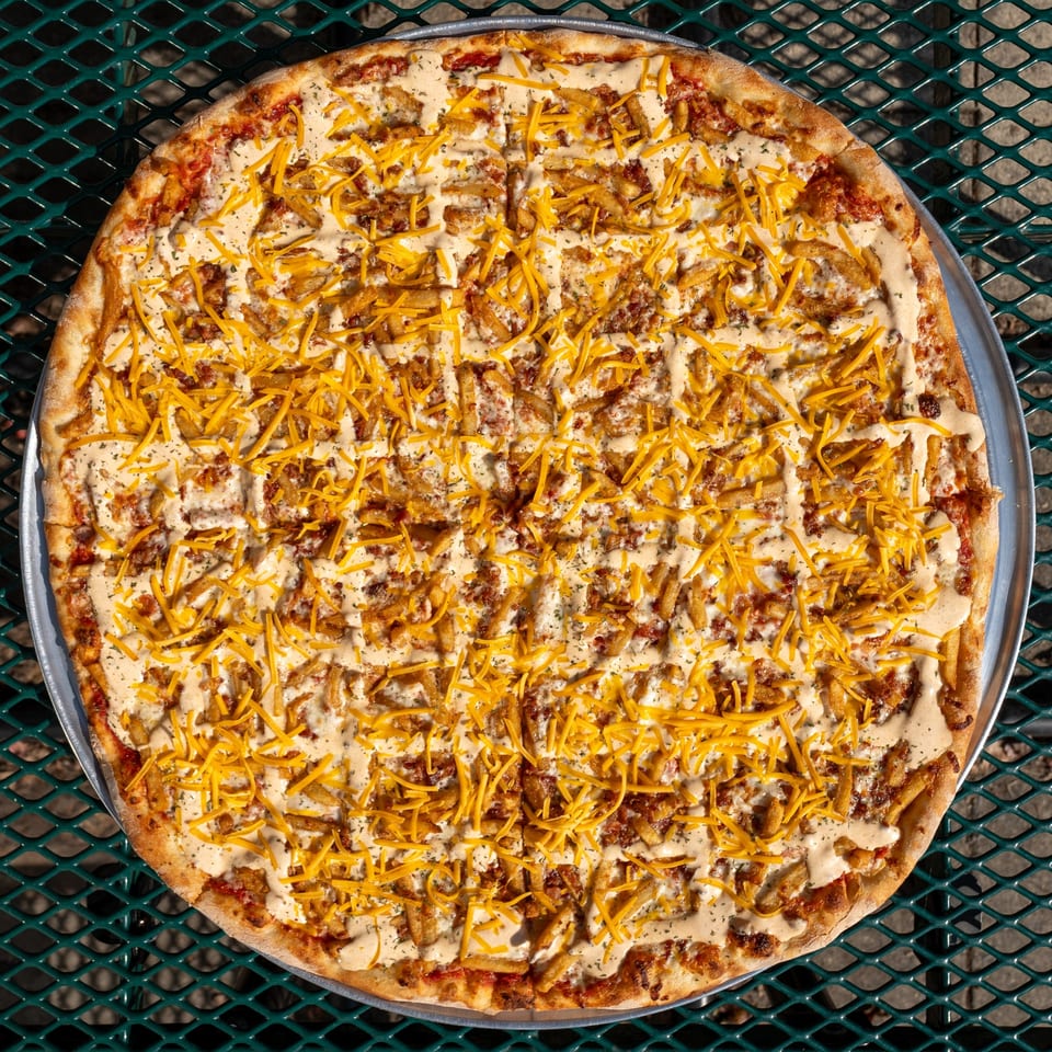 Tommyboy's Pizza with fries, shredded cheese, and a creamy sauce on a metal table.