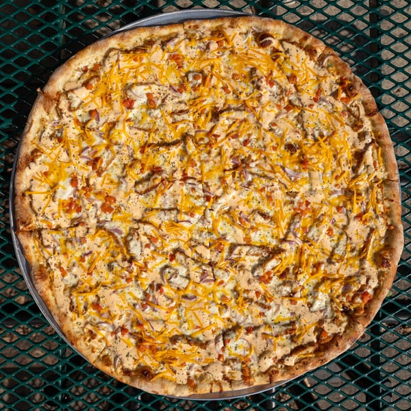 Tommyboy's Pizza with white sauce, shredded cheese, red onions, and diced tomatoes on a metal table.