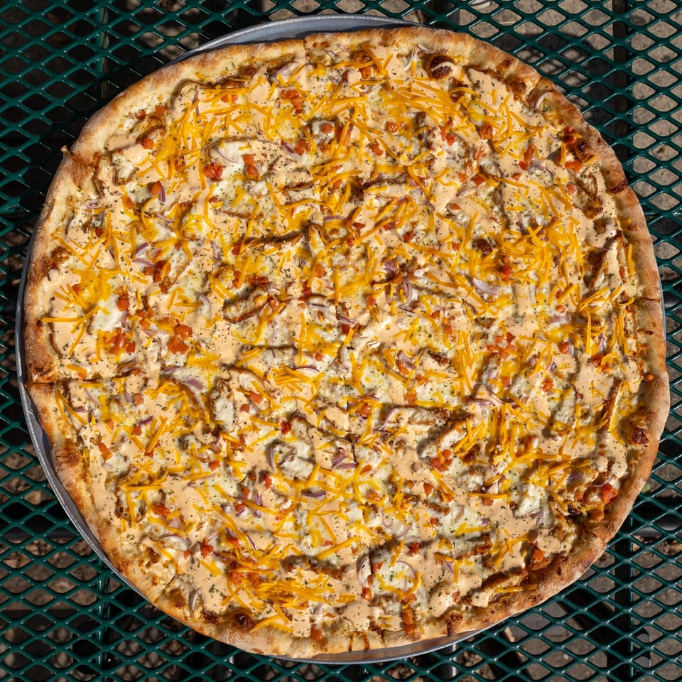 Tommyboy's Pizza with white sauce, shredded cheese, red onions, and diced tomatoes on a metal table.