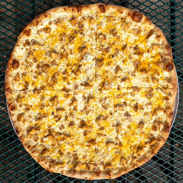 Tommyboy's Pizza with white sauce, chicken, and shredded cheddar cheese on a green metal table.