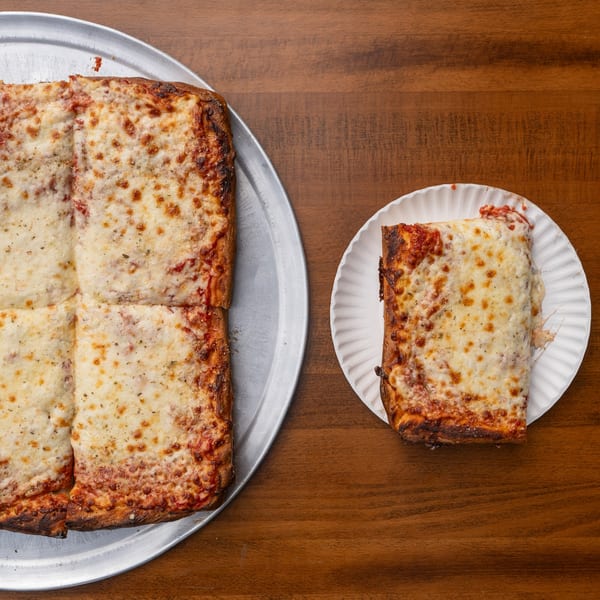 A large square Tommyboy's Pizza on a metal tray next to a single slice on a paper plate.